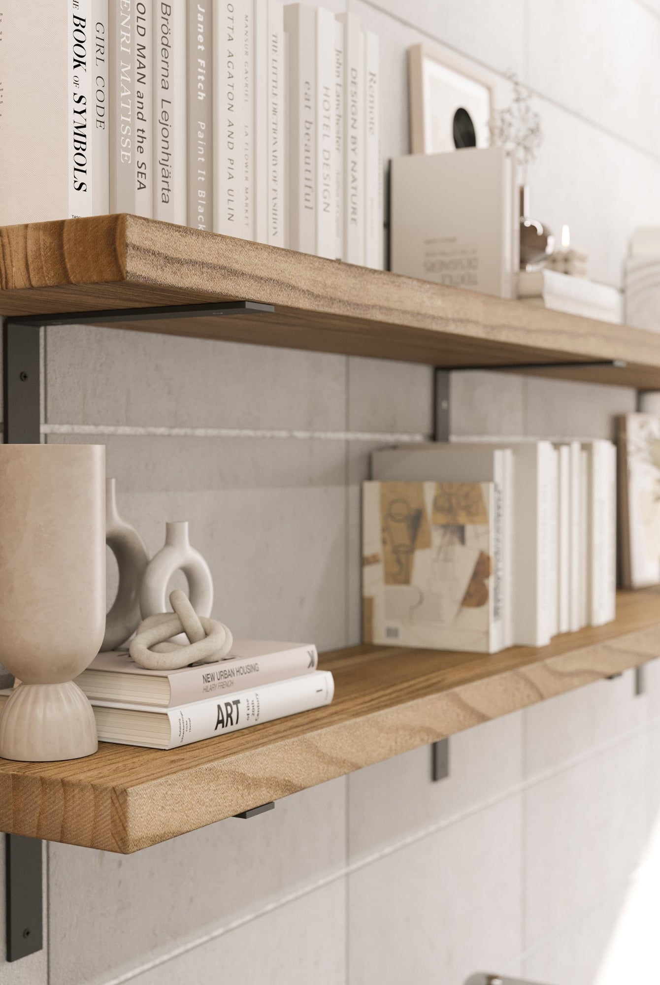 Two wooden floating shelves mounted on a white tiled wall with black metal brackets. The shelves display a minimalist arrangement of books, vases, sculptures, and framed artwork in neutral tones, creating a modern aesthetic.