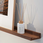 A modern diffuser with reed sticks on a 72 inch floating shelf walnut beside an abstract framed artwork, creating a serene atmosphere.