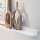 Two unique vases and a stylish art frame on a wall shelf white casting shadows on a white wall.