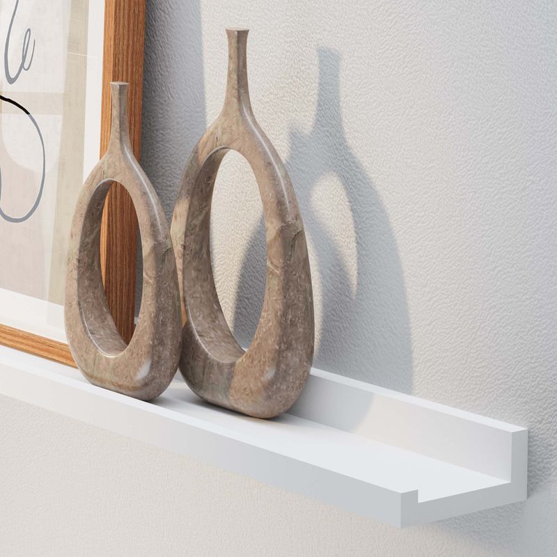 Two unique vases and a stylish art frame on a wall shelf white casting shadows on a white wall.