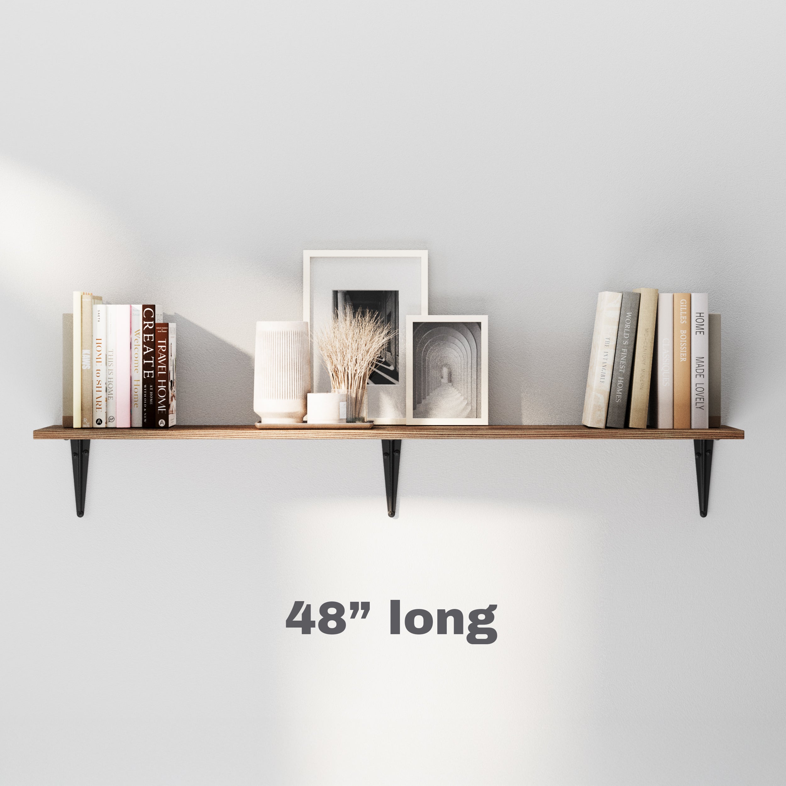 48" long dark wood shelf mounted with black brackets on a light wall. Decorated with neutral-toned books, framed art, and dried botanicals, adding simple and modern charm to any interior.
