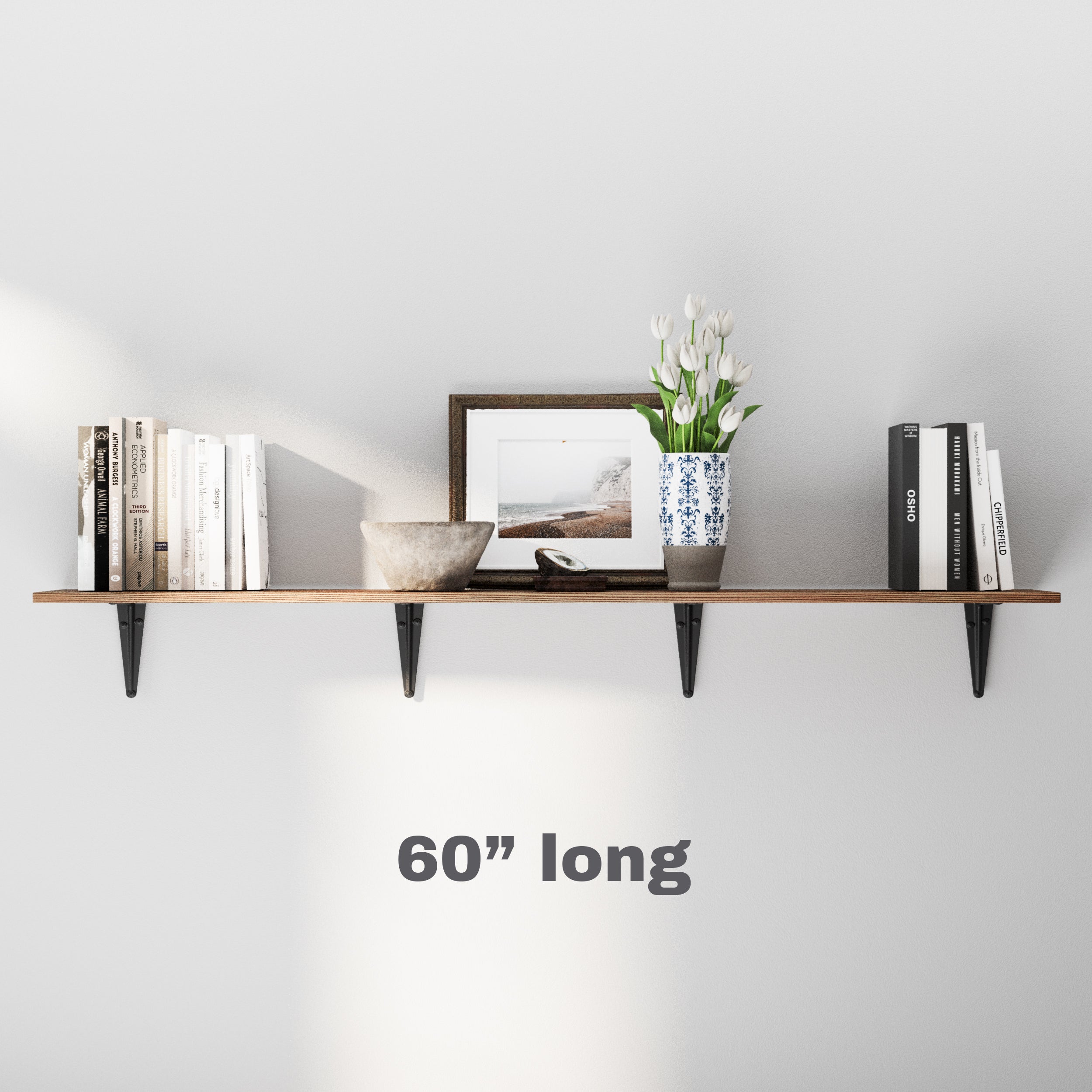 A 60" long wooden wall shelf in dark walnut finish with black metal brackets. Styled with books, a photo frame, a stone bowl, and a vase of tulips for a clean, balanced living space.