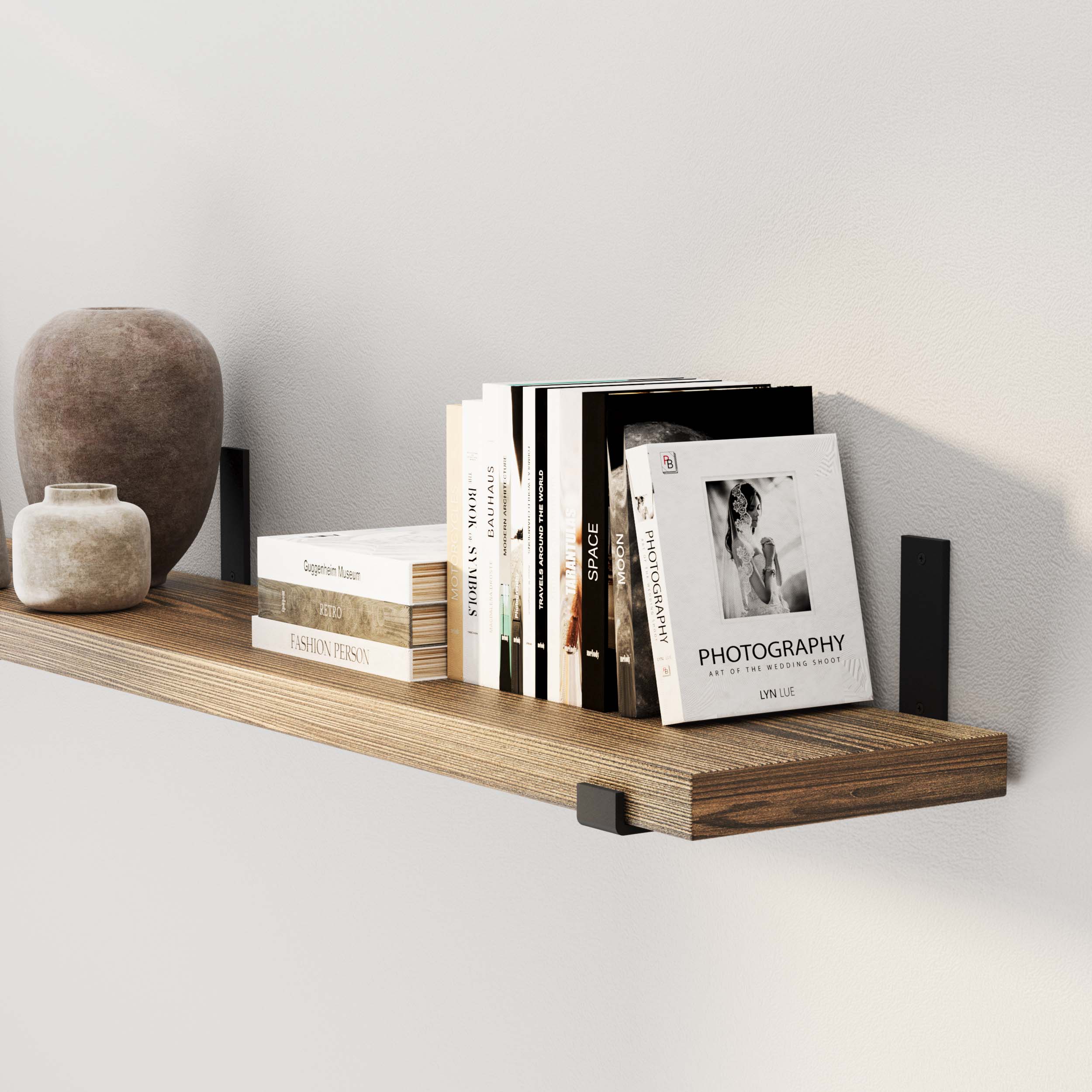 A bookshelf with books and a vase casts a shadow on a white wall.