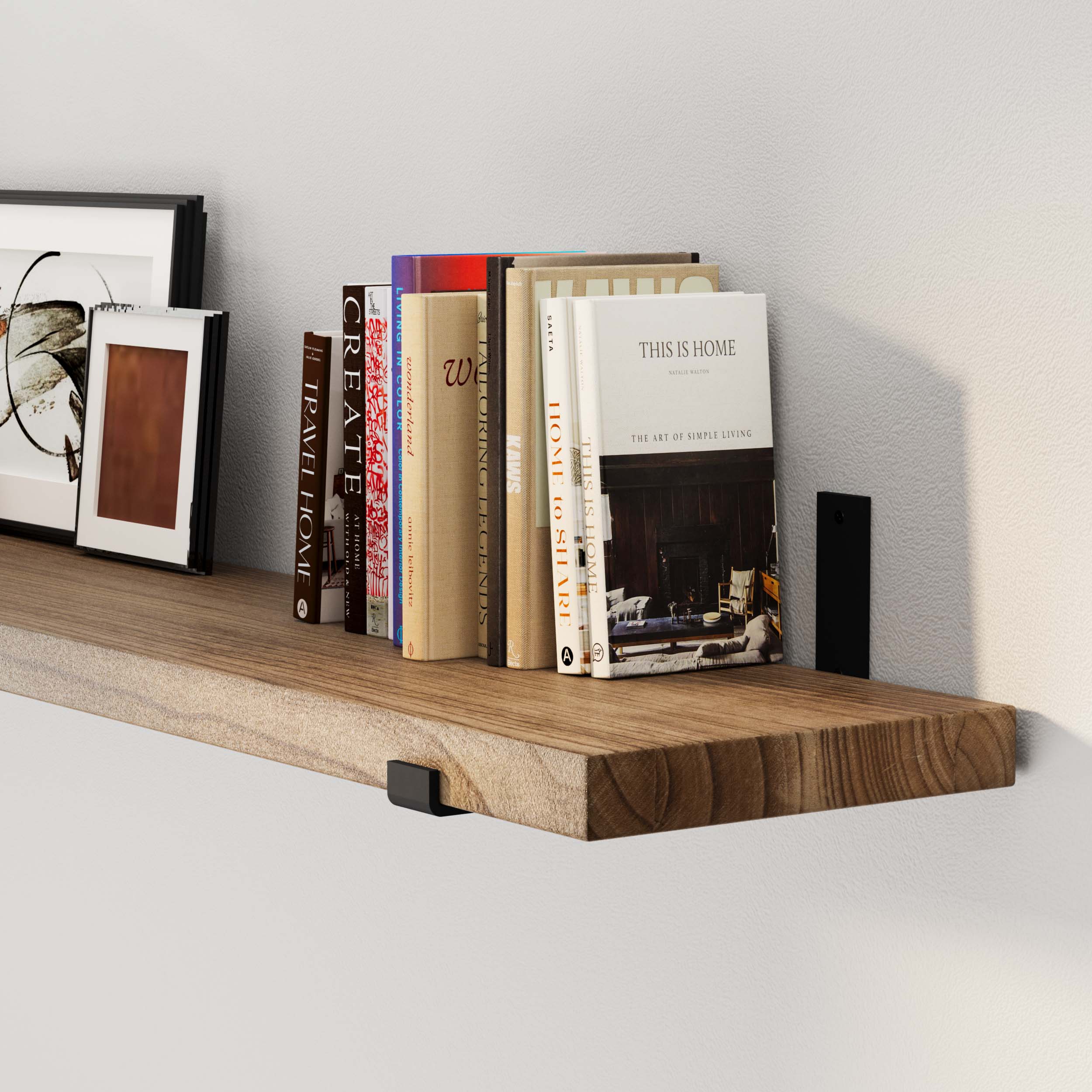 A wall shelf with assorted books and framed art against a white wall, close-up view.