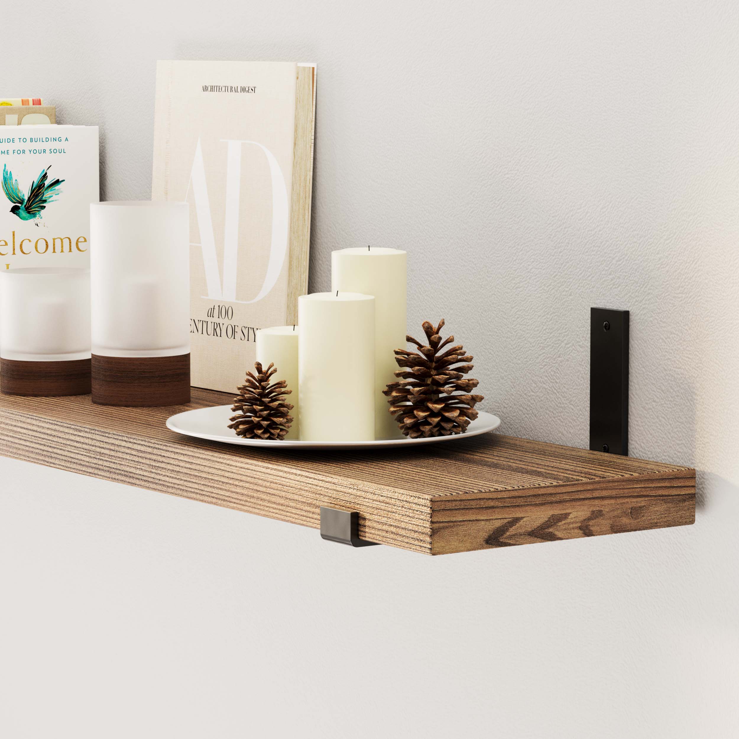 Candles and books on a bookshelf wall with black brackets.