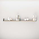 Long, narrow shelf burnt mounted on a wall displaying an arrangement of books, sculptures, and small pots.