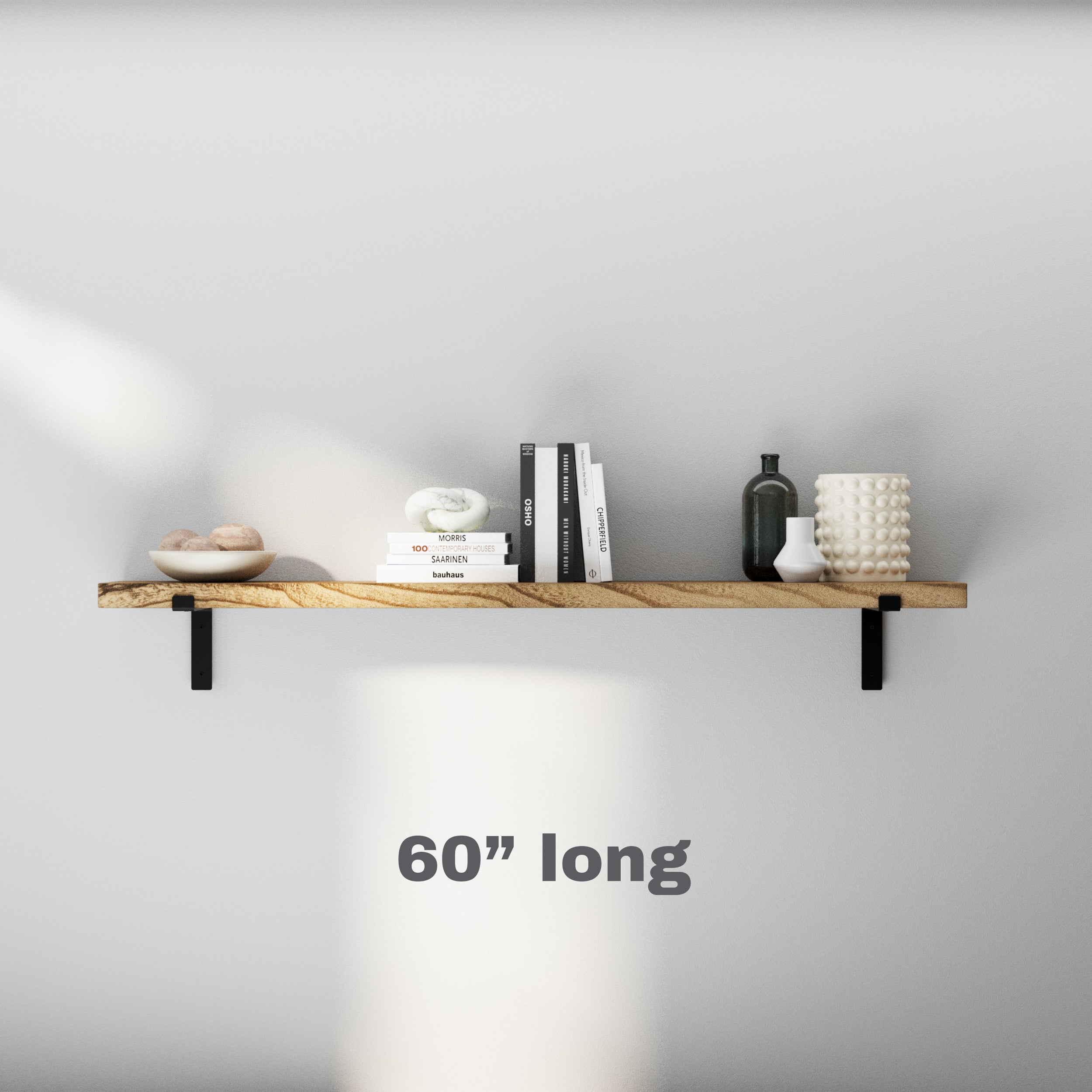 A 60 inch floating book shelf with black brackets, styled with books, a clock, vases, and decorative pieces on a white wall.