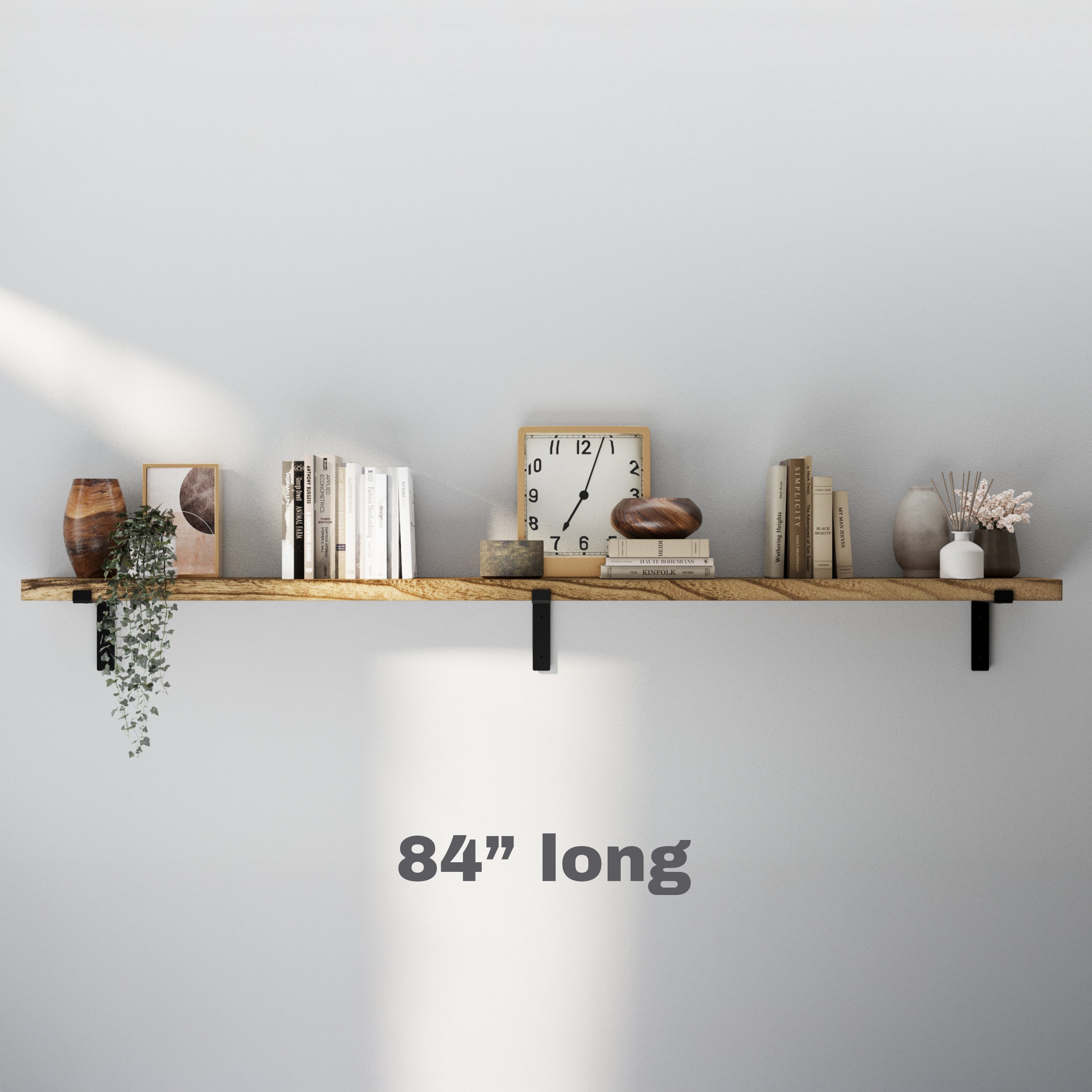 A minimalist 8 inch extra long floating wall shelf with black brackets, decorated with books, vases, a clock, and a small plant, enhancing a modern wall.