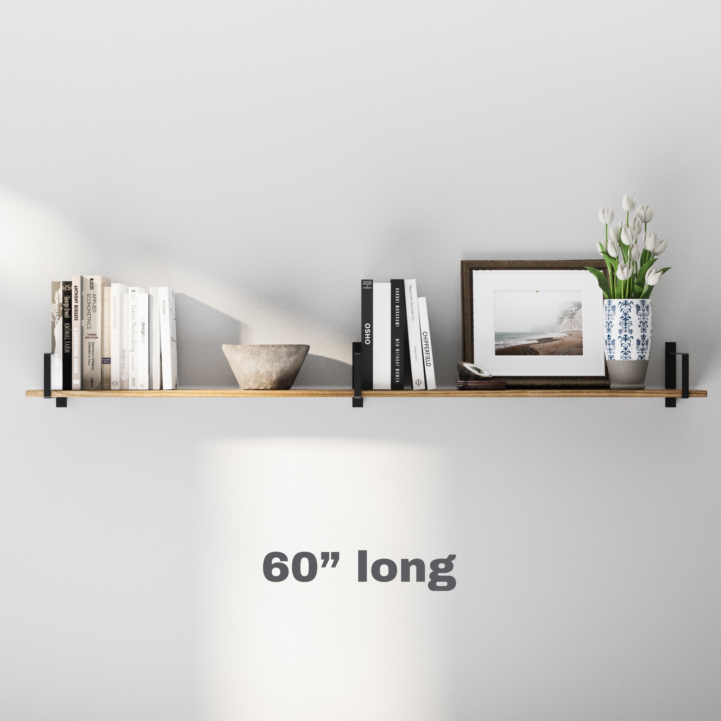 A 6 inch long floating book shelf with black metal brackets, holding books, a framed picture, a decorative bowl, and a vase with white tulips, blending minimalist and modern styles.