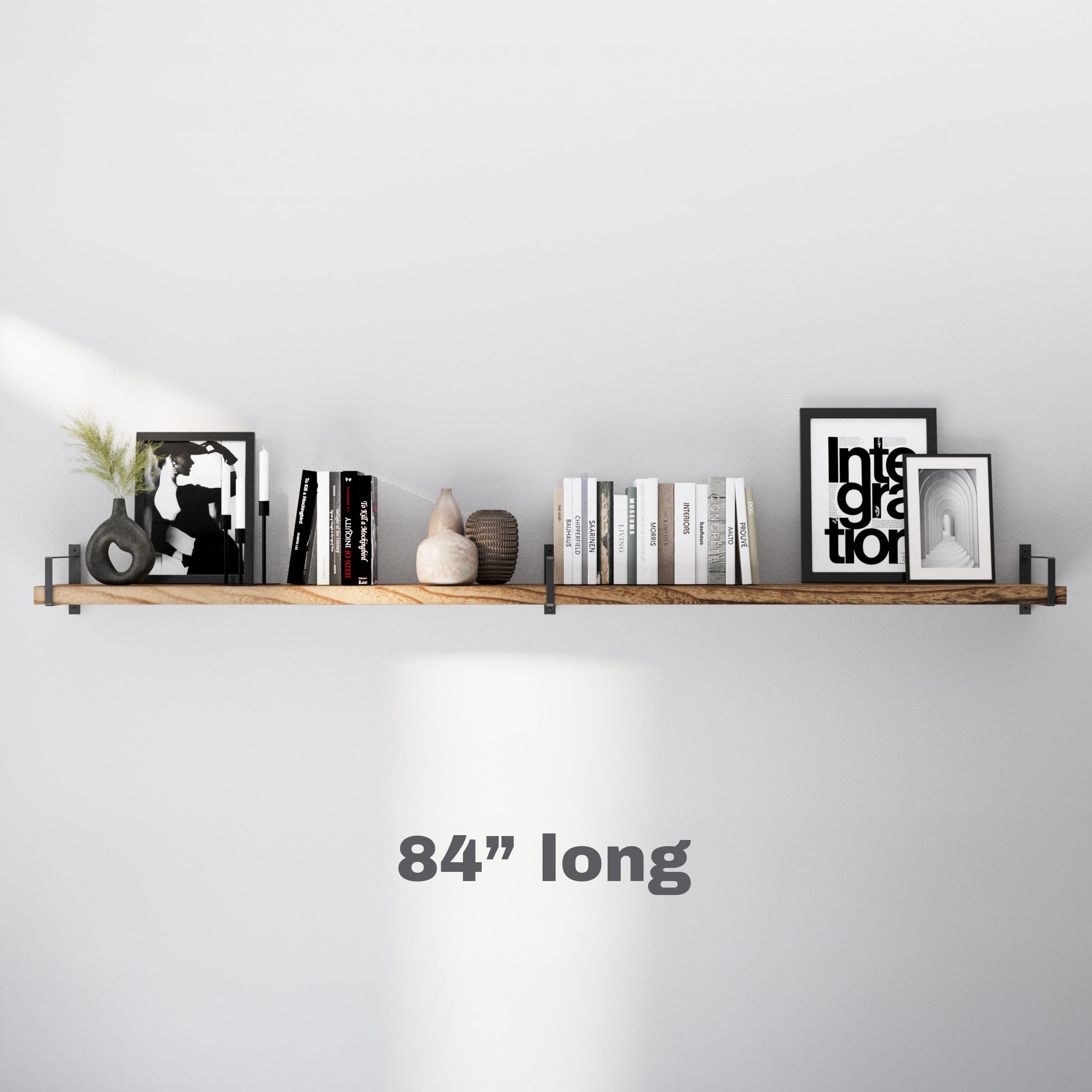 A 84 inch extra long wooden wall shelf with metal brackets, showcasing a modern aesthetic. Decorated with neutral books, black-and-white art, and ceramic pieces, it creates a sleek and balanced display.