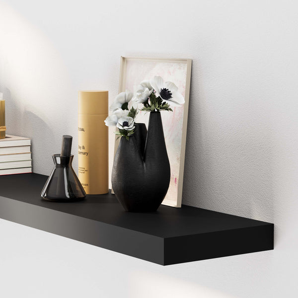 An elegant black wall shelf displays books, a decorative hourglass, and a framed artwork in a serene setting.