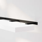 A white foating shelf for wall with a black hidden bracket mounted on the wall, highlighting its sleek design and sturdy brackets.