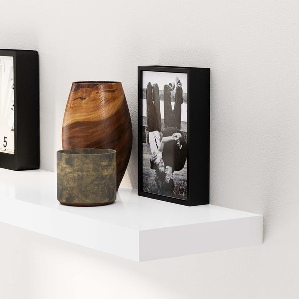 White floating shelf displaying a wooden bowl, brass pot, a clock, and a framed black and white photo.