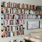 A large wall installation of black shelves filled with books, transforming the room into a spacious, organized home library that enhances the room's décor.
