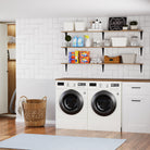 Pantry shelves above a washer-dryer set, holding detergent, towels, and storage bins—adding vertical storage and charm to a crisp, clean laundry room.