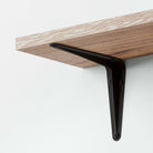 Sturdy black I metal bracket securely supporting a wood wall mounted shelf for modern wall-mounted shelving.