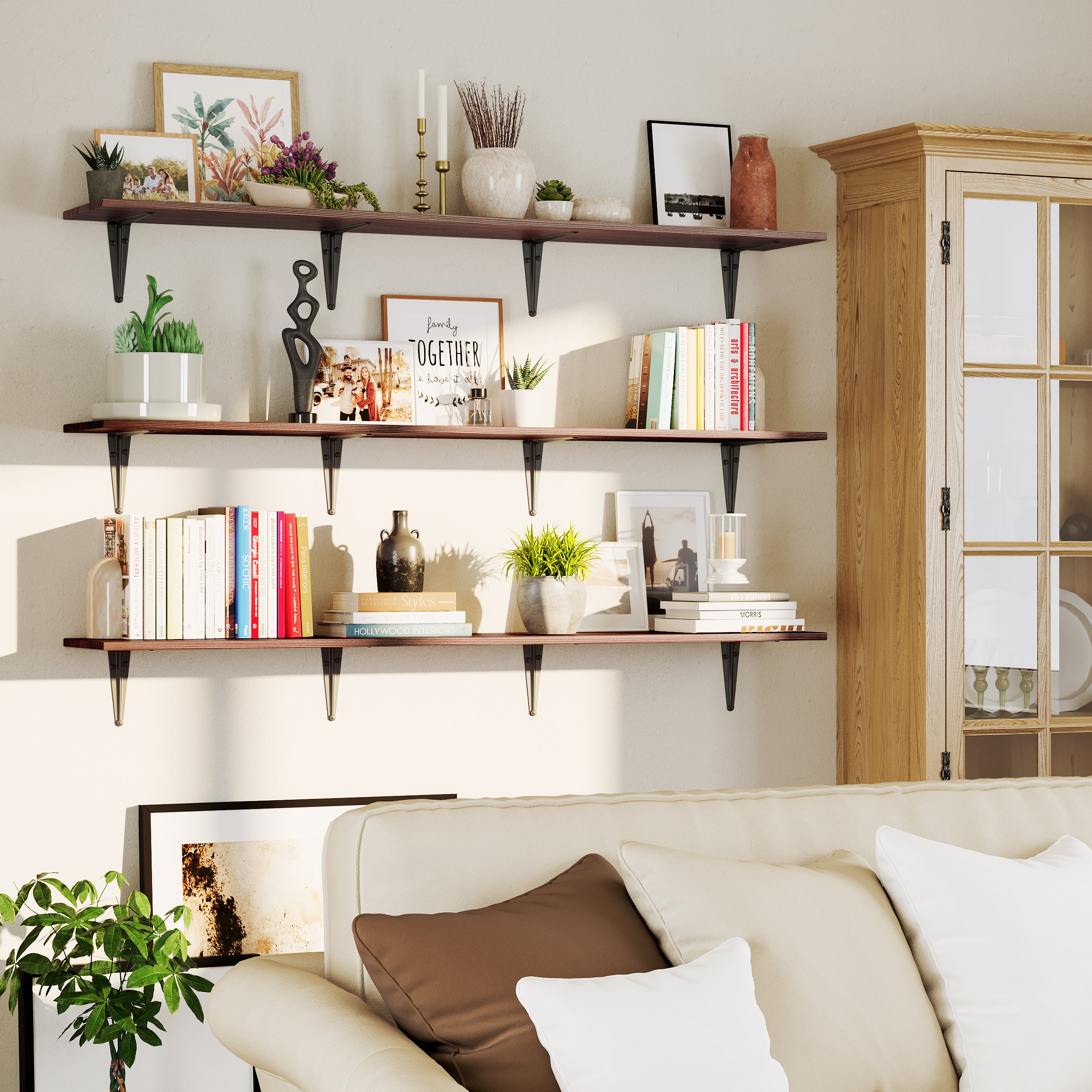 Rusticfloating shelves above a cream couch display framed art, candles, books, and lush plants. A warm, inviting living room corner with soft daylight and a rustic wood cabinet.