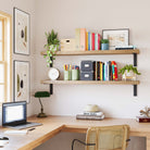 Office-inspired wall mounted shelves styled with plants, books, and storage boxes. The space is bright and organized, featuring a wooden desk and green accents.