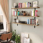 Three-tiered rustic wall bookshelves styled with books, vases, and decor. The layout complements a modern study setup with plants, a desk, and earthy tones.