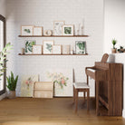 A chic living area with white walls, long shelves with framed botanical prints, next to a piano and modern decor elements.