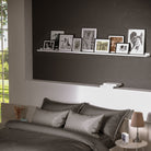 72 inch foating shelf with frames on a dark wall above a bed.