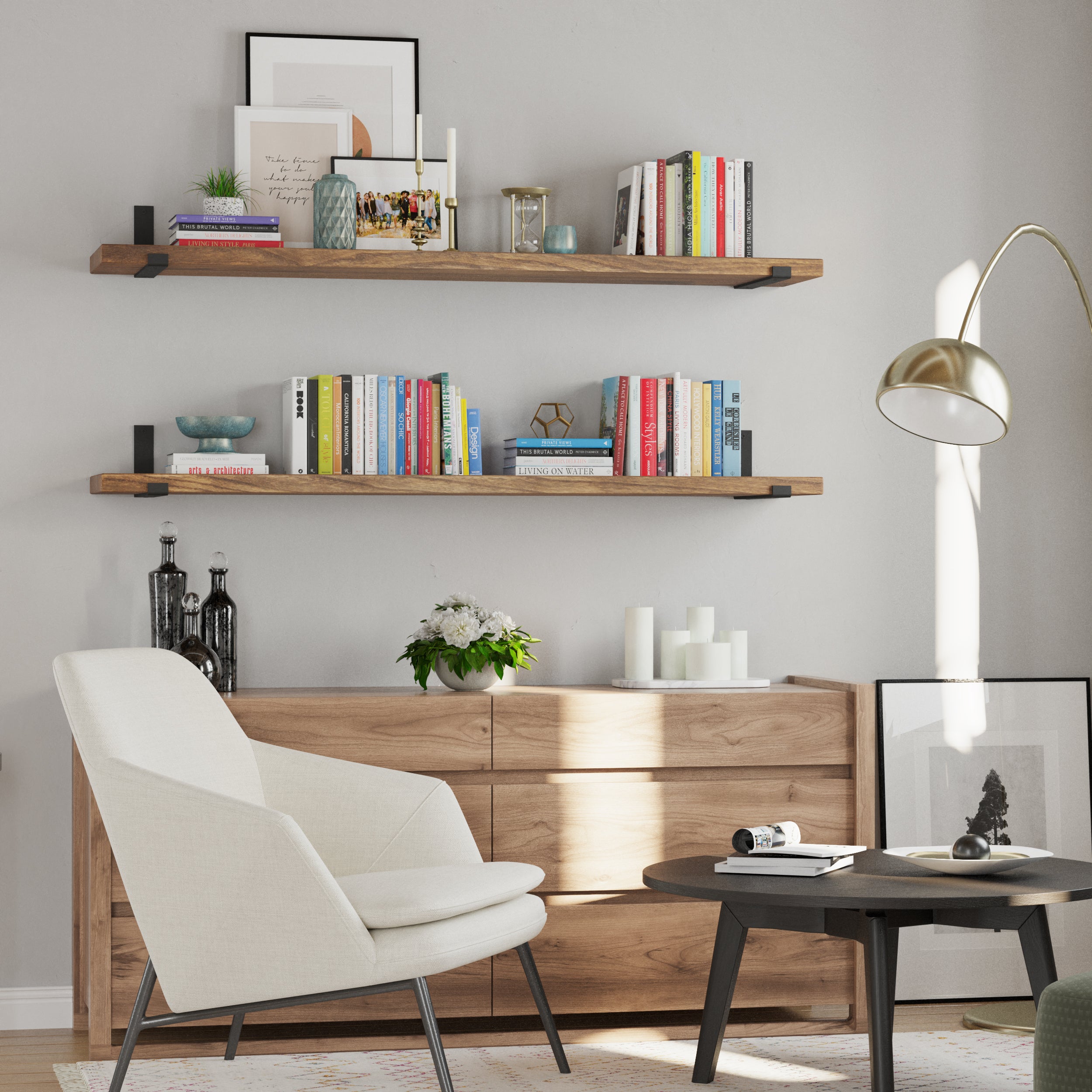 A cozy reading corner featuring two long display shelves in rich provincial finish with books and decor above a wooden dresser. A white armchair, black round coffee table, and gold floor lamp complete the modern, elegant design.