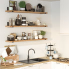 A modern kitchen with three wooden farmhouse shelves holding glass jars, ceramic bowls, utensils, and plants. Below, a black sink with a gooseneck faucet is set on a light wood countertop, with dishware and a stove nearby.