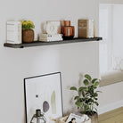 A floating ebony shelf decorated with books, vases, and ornaments against a cozy reading nook with a potted plant below.