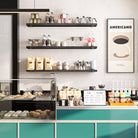 Floating wall shelves displaying coffee-related items, glass jars, and decor in a stylish café with a teal counter.
