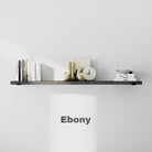 A sleek, ebony-colored 60 inch long floating shelf on a white wall, holding books, a clock, and decorative objects in a minimal style.