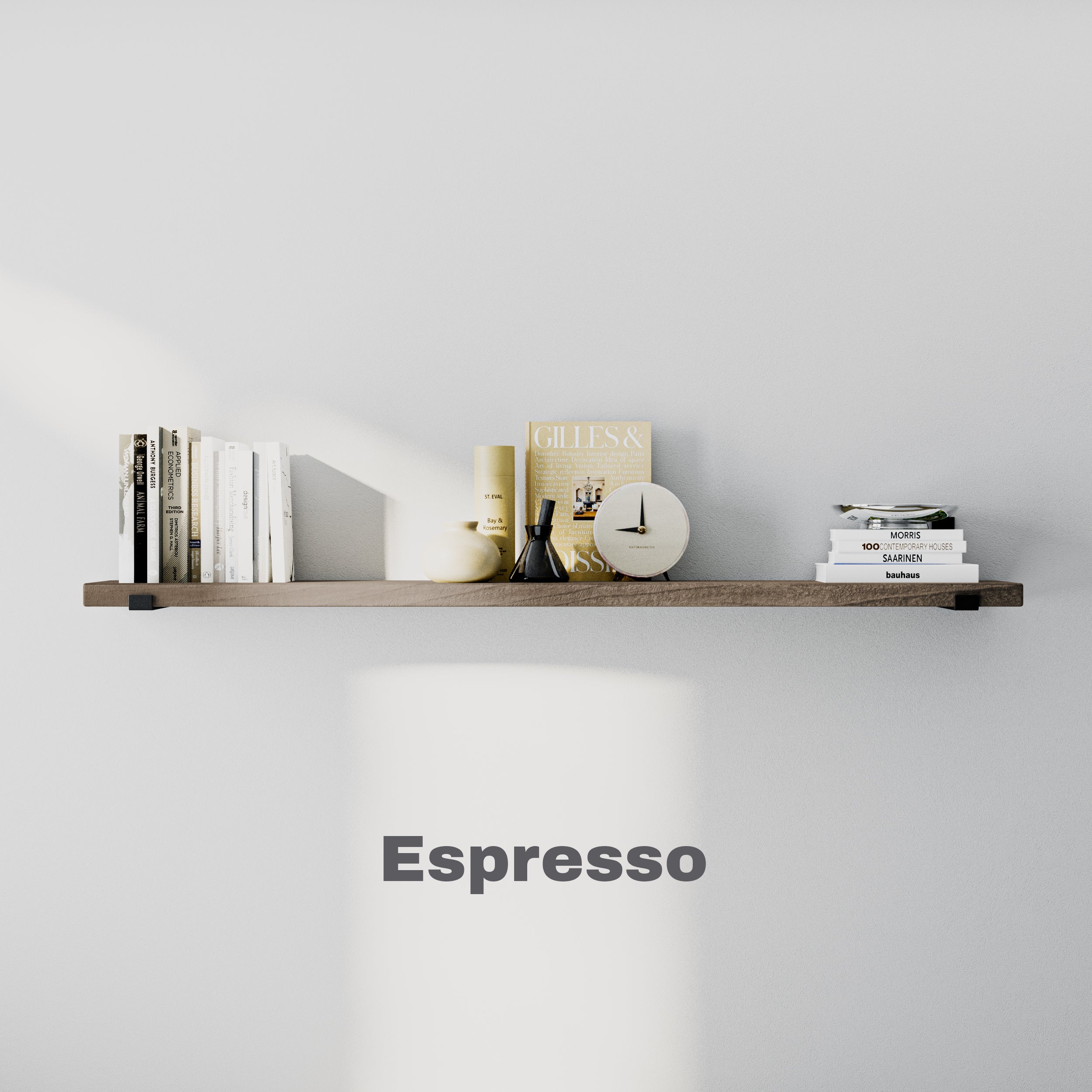 A floating wall bookshelf in an espresso finish holds neatly arranged books, a clock, decorative items, and a minimalist color scheme. The shelf is labeled "Espresso."