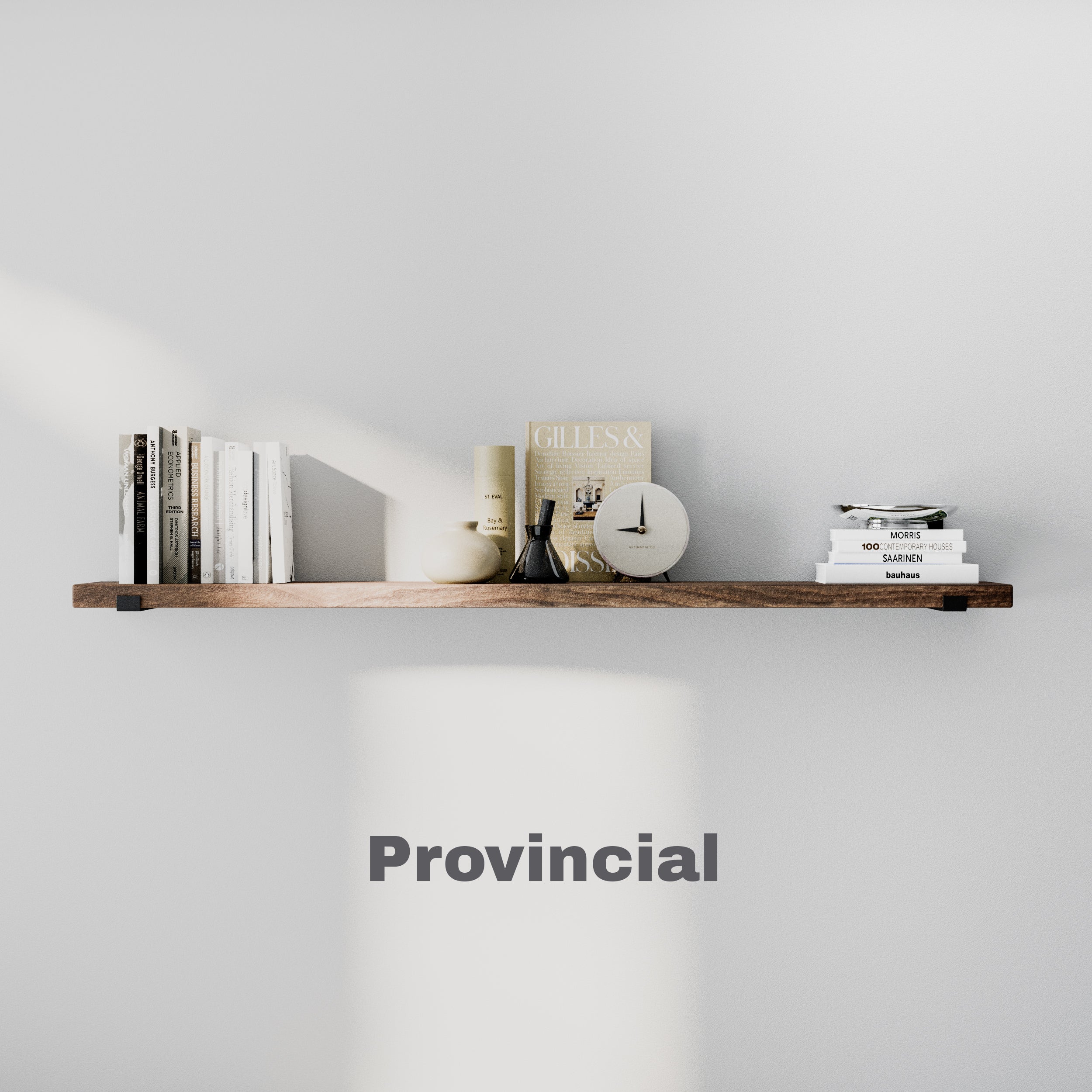 An 60 inch long display shelf in a provincial finish holds books, a clock, and decorative objects, casting a soft shadow on a white wall.