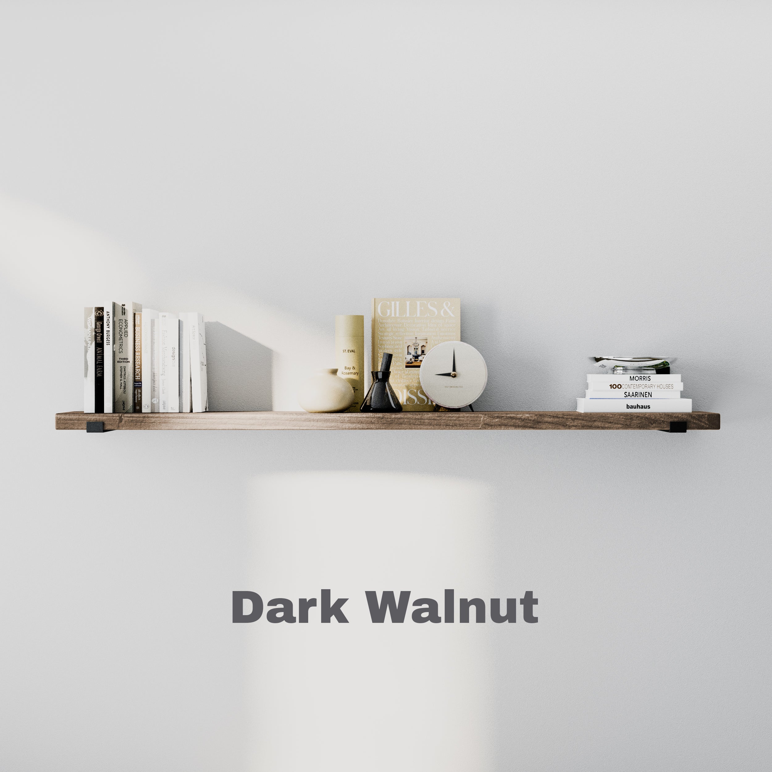 A floating bookshelf in dark walnut finish against a light wall, styled with books, a clock, and decorative items.