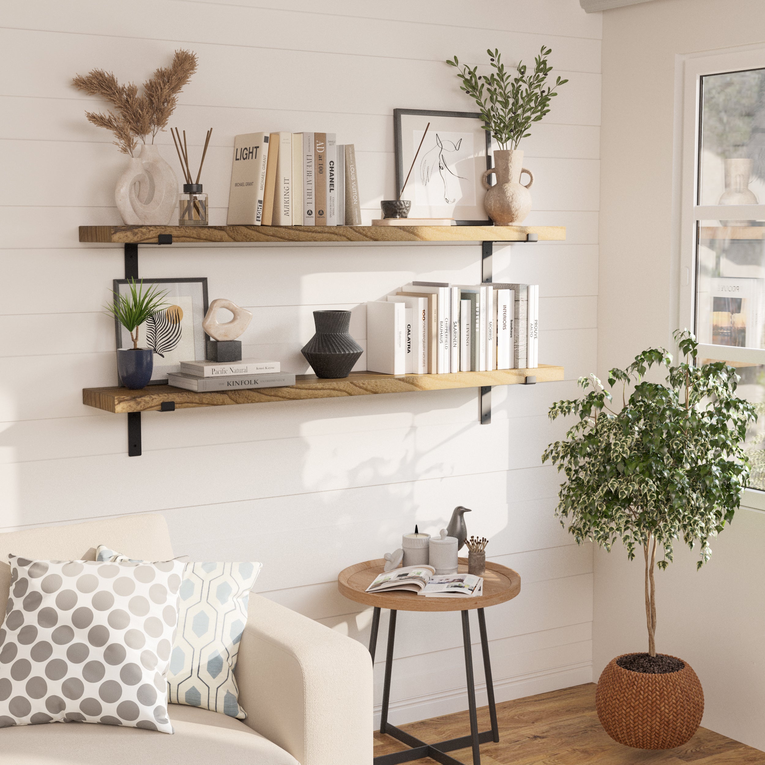 Two 60 inch long farmhouse shelves on a white wall displaying books, art pieces and vases, next to a cozy seating area with plants.