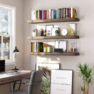 A home office wall features three espresso-colored floating shelves organized with books, pencils, clocks, and décor—enhancing productivity with modern charm.