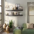 Two floating ebony-finish shelves styled with candles, framed photos, books, and glass decor. Accents a cozy corner with a green couch and decorative floor vases.