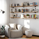 A reading nook with three tiered long pipe shelves, packed with books and plants, set above a plush armchair and a pouf for a warm, relaxing corner.