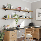 A home office with dual long wooden shelves above a black desk, decorated with books, plants, and minimalist art, creating a productive and aesthetic workspace.
