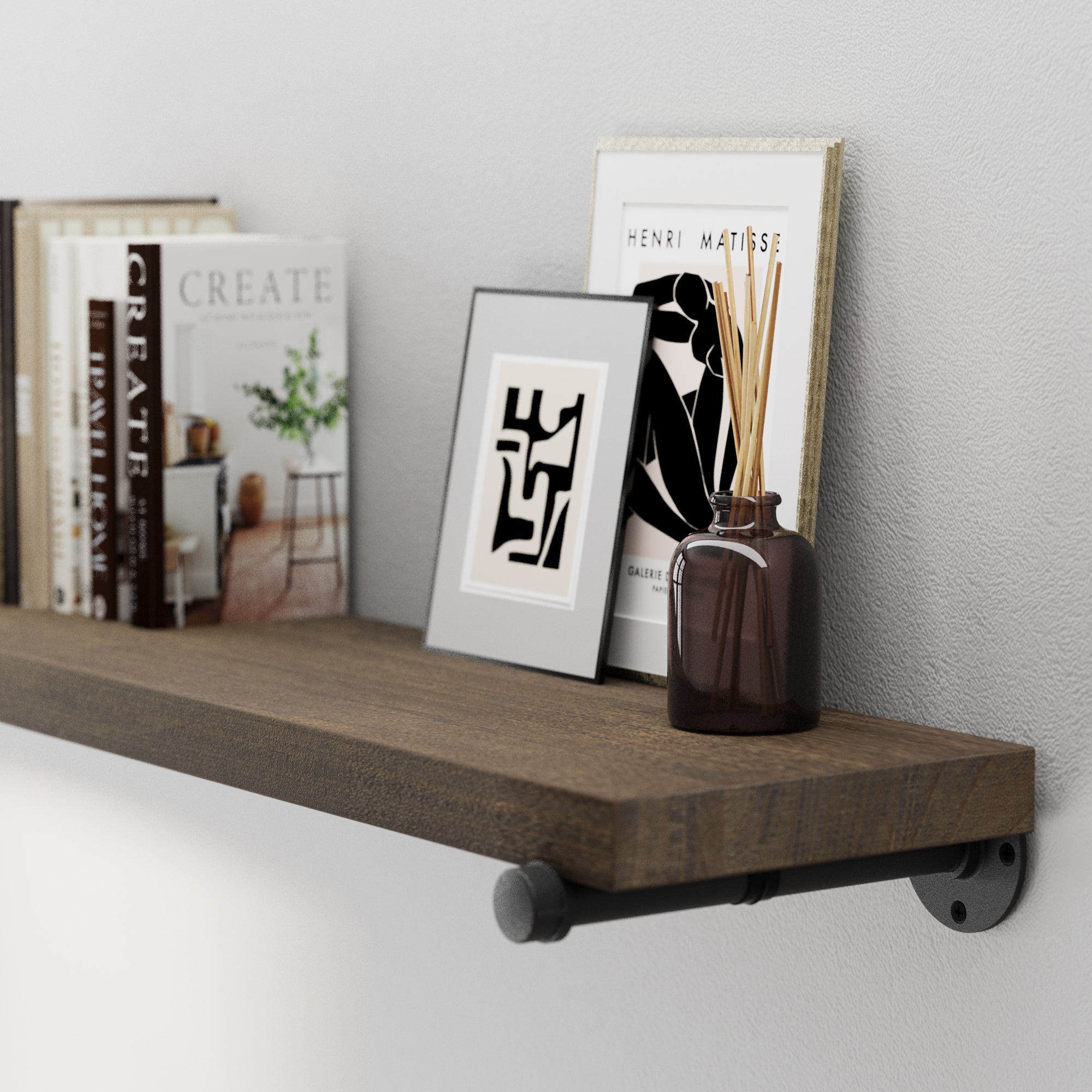 A real wood and 60 inch industrial pipe shelf featuring rustic wood texture and industrial pipe brackets. Styled with books, framed wall art, and diffuser décor, ideal as a living room shelf or office wall storage.