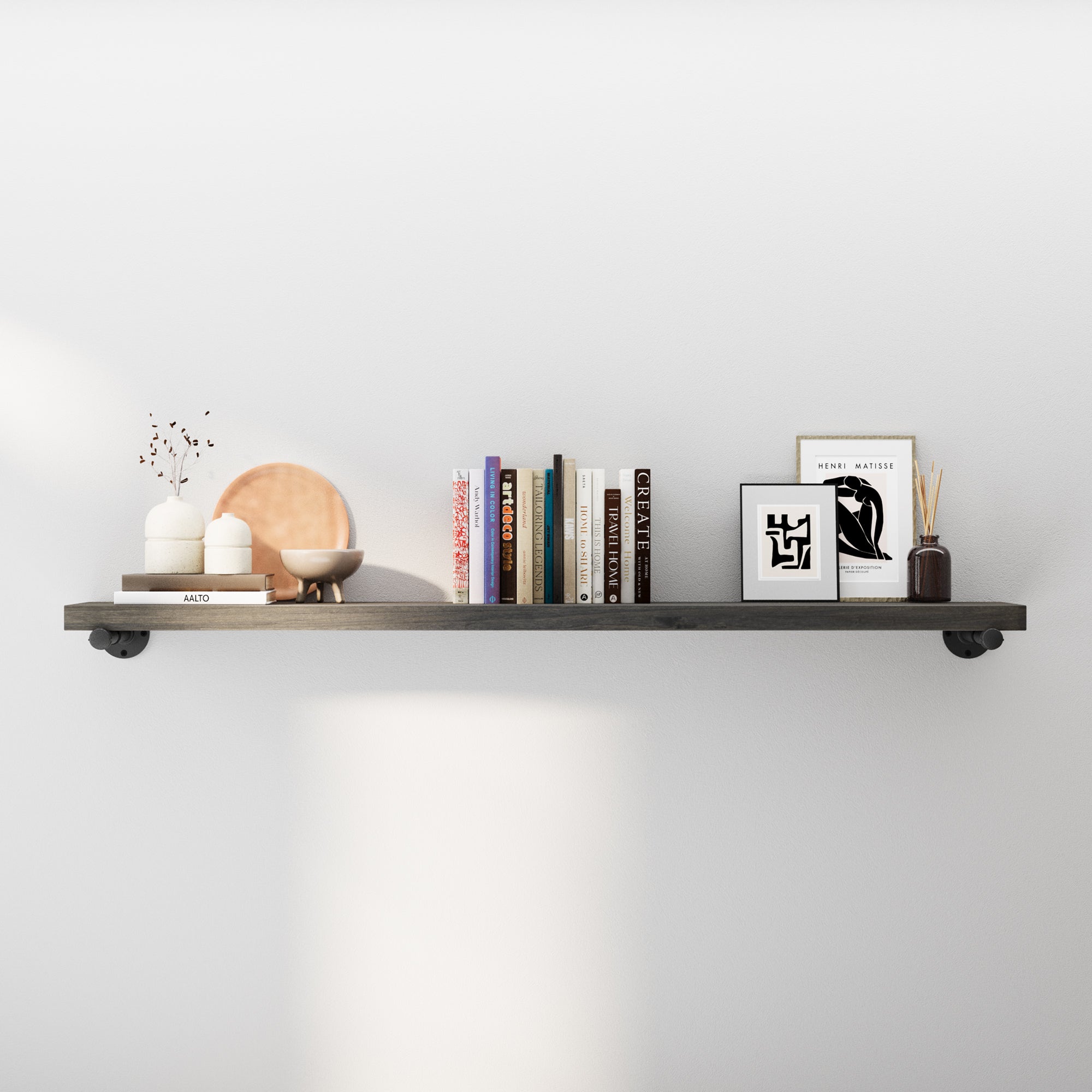 60" industrial pipe shelf in a rich ebony finish styled with books, framed art, and modern décor. Rustic wood wall shelf with heavy-duty black pipe brackets adds farmhouse charm, perfect for living room wall décor, books, and storage.