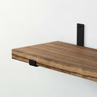Close-up of a wooden shelf supported by a black rectangular shelf bracket.