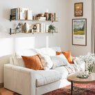 A cozy living room with two boho shelves, showcasing books, ceramics, and plants above a white sofa adorned with warm-toned pillows and a Van Gogh print.