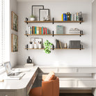 A bright home office with three60 inch long rustic home office shelves, storing books, decor, and greenery above a sleek white desk with a leather chair.