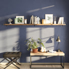 A single long shelf on a navy wall adds striking contrast and modern appeal. Styled with books, frames, and candles, it creates a functional focal point above a minimalist wooden console.
