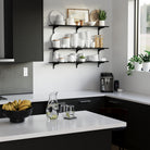 Kitchen floating shelves stocked with white dishes, green plants, against a clean backdrop.