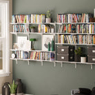 Two large multi-shelf units mounted on a green wall, filled with books, frames, plants, and accessories, creating a stylish reading nook.