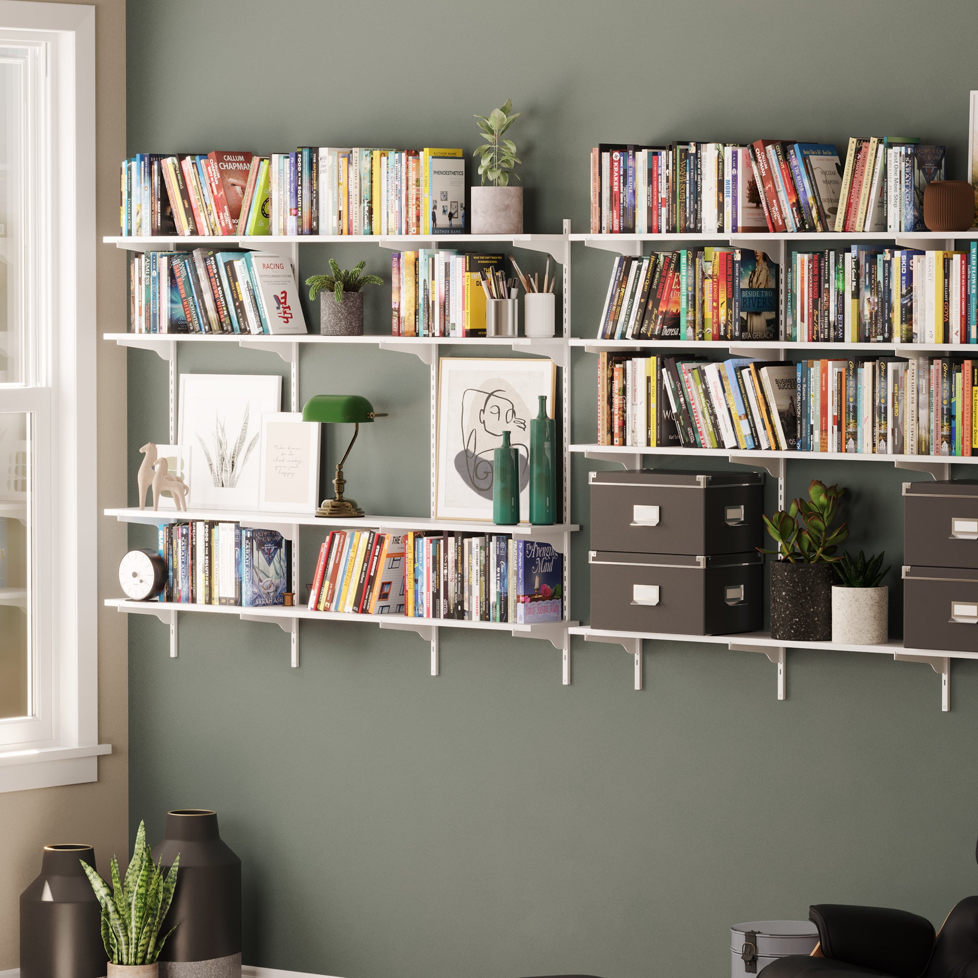 Two large multi-shelf units mounted on a green wall, filled with books, frames, plants, and accessories, creating a stylish reading nook.