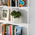 The wall book shelf corner showing its sturdy white metal bracket and neatly placed ceramic bowl and decor accents.