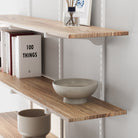 Paulownia wood shelving unit with white adjustable brackets holding decorative items against a white wall