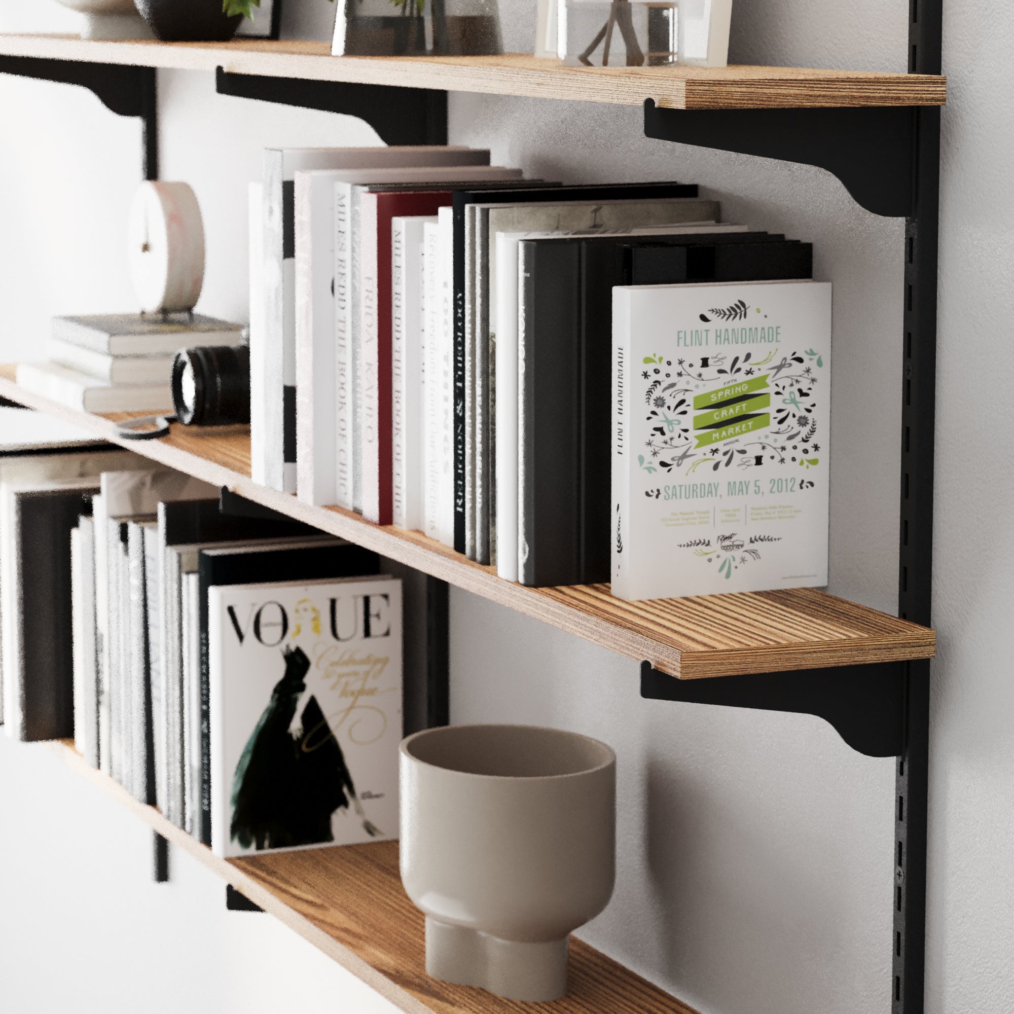 Floating bookshelf with adjustable rail brackets in black color, holding books and a vase against a white wall